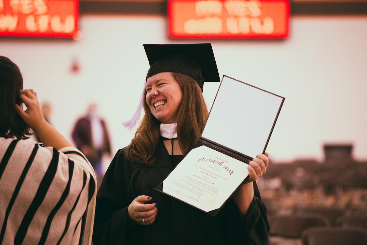a doane university student posing and smiling during graduation wearing the traditional robe and cap and holding her diploma.