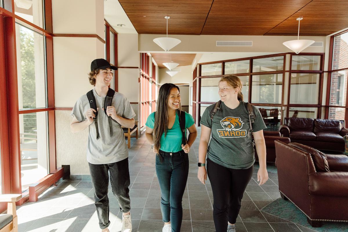 three Doane students walking through a campus building, laughing, and having a conversation.